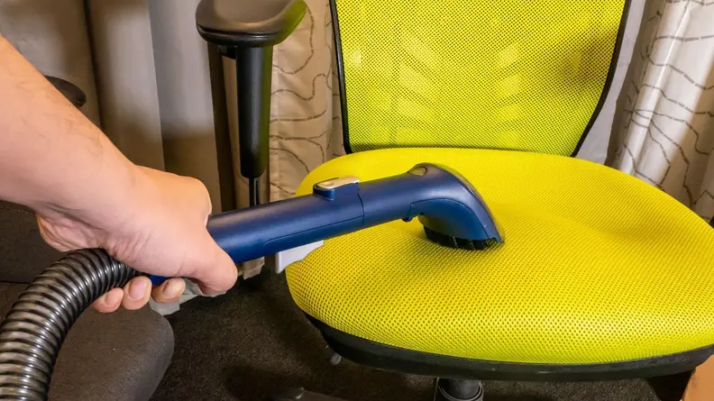 Person using hose attachment from the Eureka NEY100 carpet cleaner on the seat of a bright yellow office chair.