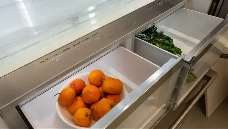 A bowl of oranges and fresh leafy greens found inside a refrigerator's crisper draw.