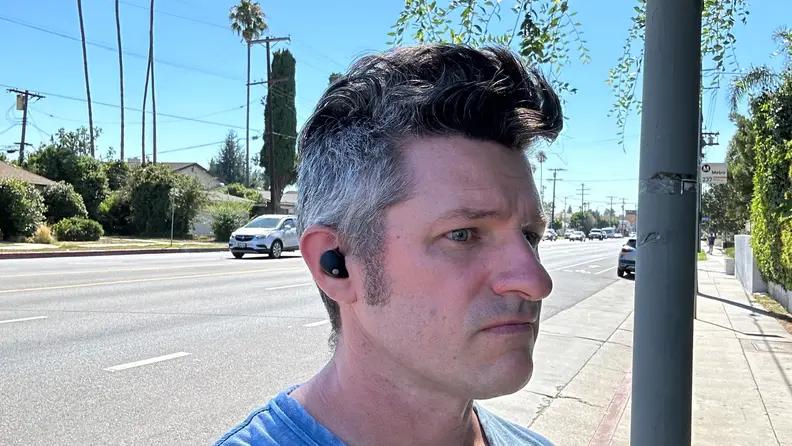 A man wearing the Sony WF-1000XM5 earbuds outside with car going by.