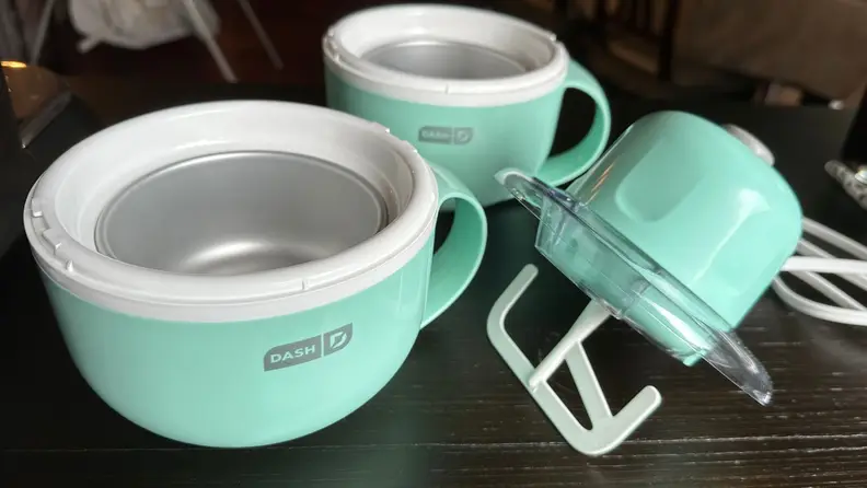 The Dash ice cream maker mug bases and motorized head on wooden surface.