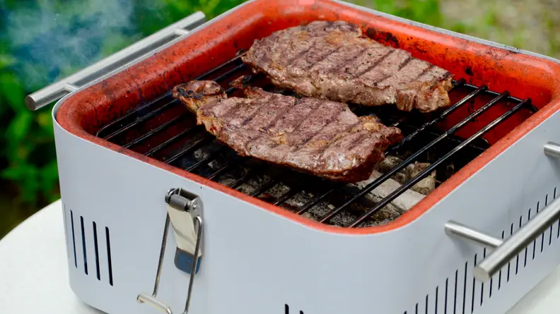 On the Everdure Cube charcoal grill in grill, there are two steaks.