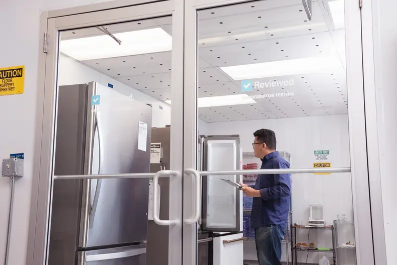 An Asian man with a clipboard stands in a room with glass walls