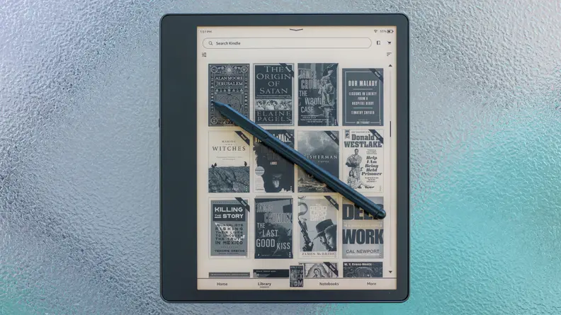 An Amazon Kindle Scribe sits on a glass table, with its Premium Pen stylus resting on top of it.