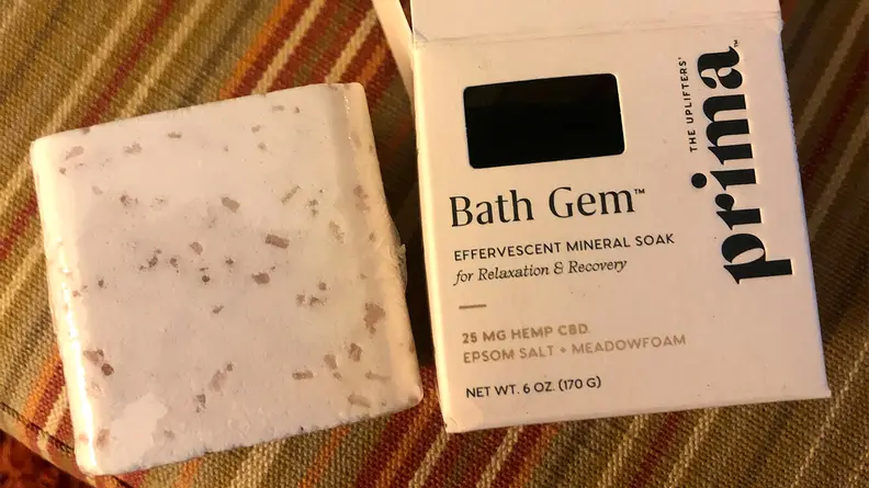 On the left, a Prima Bath Gem is photographed out of the box: a large, white square bath bomb. Right: the black-and-white packaging the Bath Gem comes in.