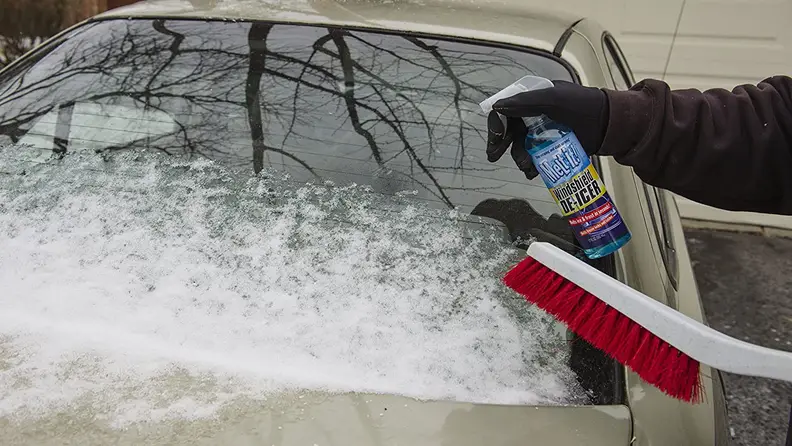 A shot of someone using a lock de-icer to de-ice a windshield.