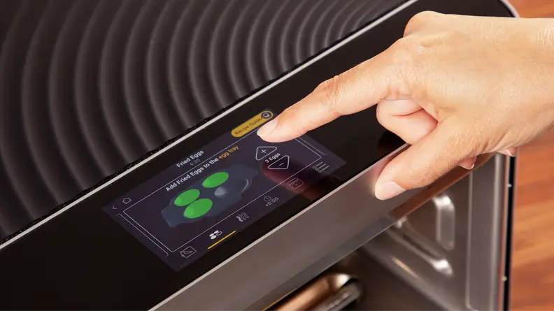 A person using their finger to navigate and select cooking settings on the touchscreen menu of the Brava Glass Oven