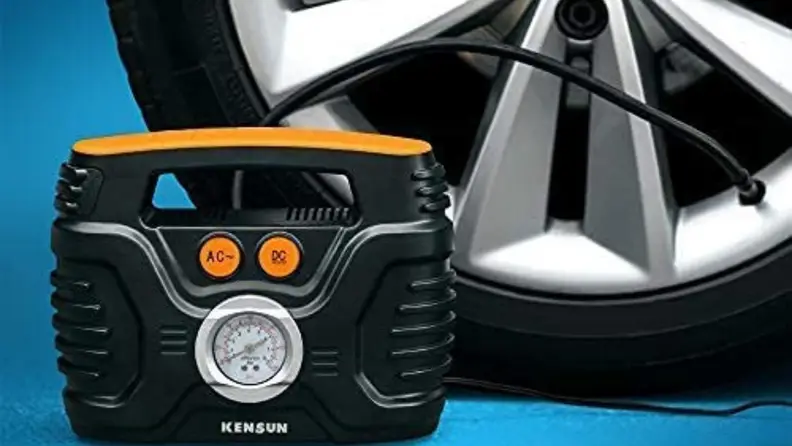 Mini compressor in front of car tire on blue background