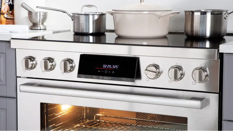 The Bosch HIS8655U 36-in Induction Range shot up close, with cookware on top and the oven light on