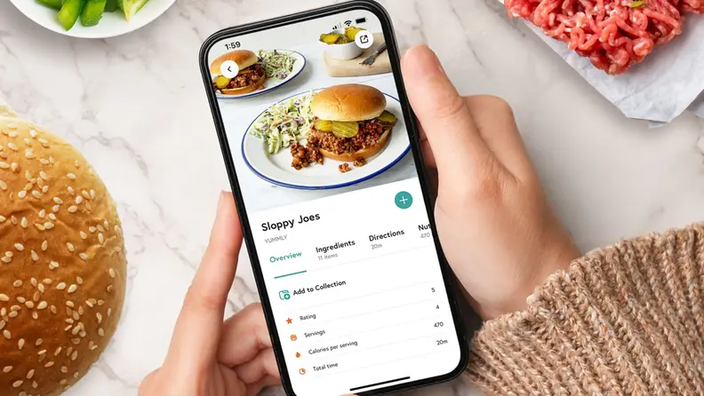 A hand holding a smartphone displaying the Yummly app.