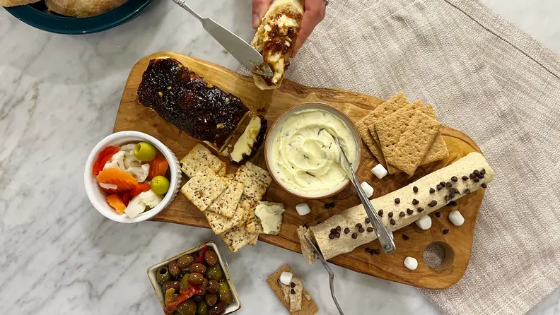 Hand spreading butter on baguette slice, next to a butter board.