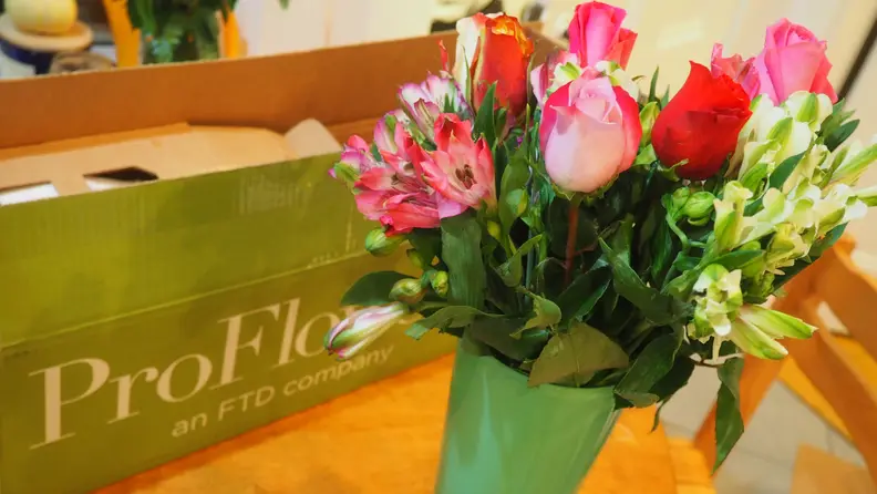 Roses in green vase on table with ProFlowers box