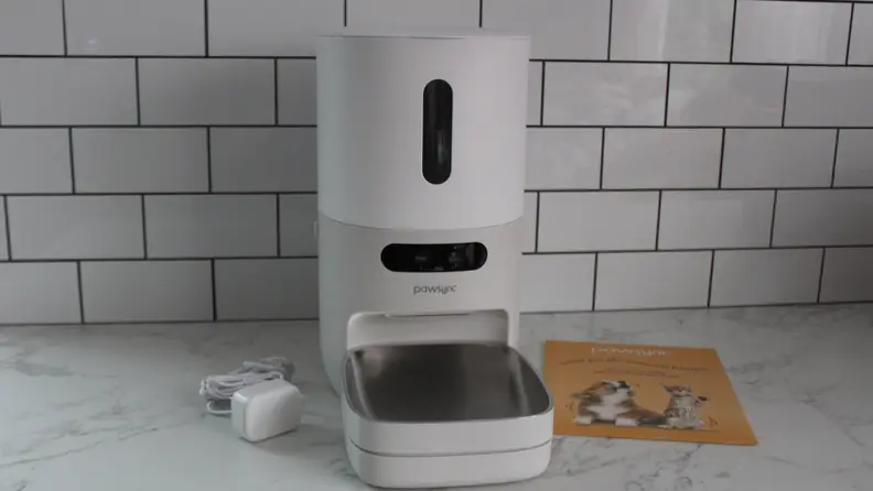 The PawSync Smart Pet Feeder next to instruction guide and the power cord on top of a marble countertop.