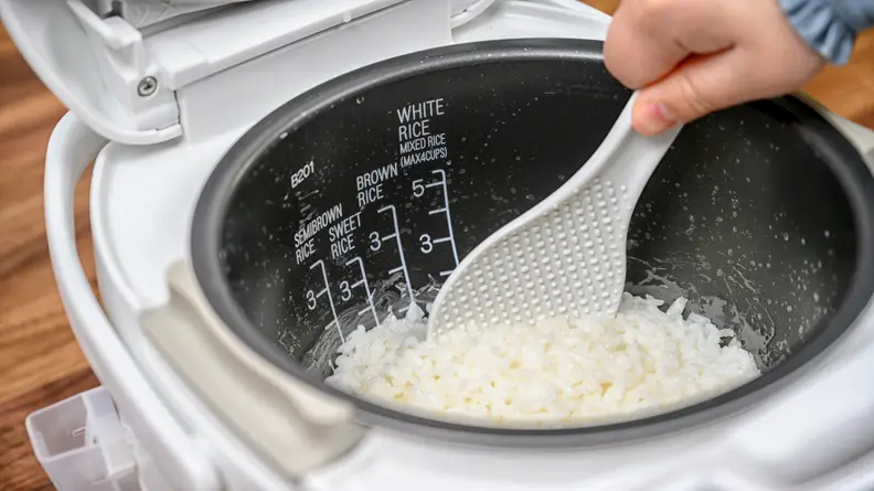 Hand stirring rice in a rice cooker.