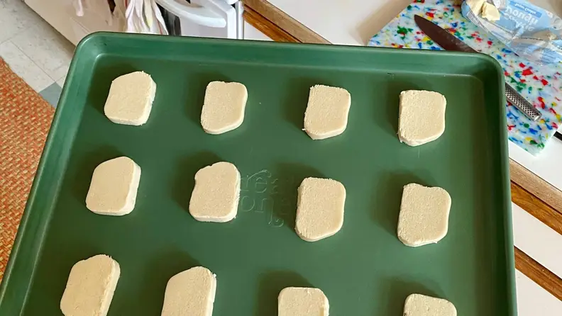 Raw sugar cookie dough evenly spaced on a green baking sheet, ready to go into the oven.