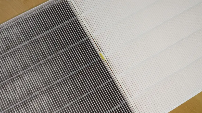 A used HEPA filter darkened by dirt and dust compared to a new clean filter.