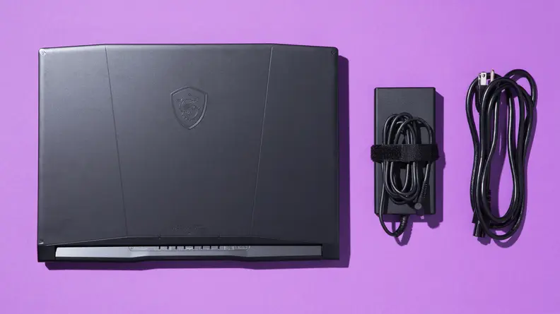A black laptop and its black charging cables against a purple backdrop.