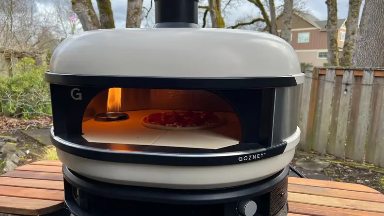 Pizza pie inside of Gozney Dome Pizza Oven on stand with wooden side tables.