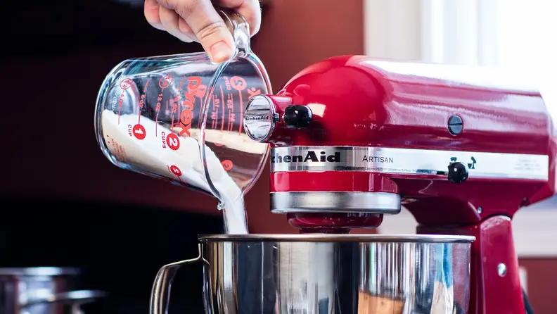 A hand pouring flour into a red stand mixer