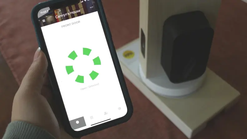 A hand holding a phone displaying the app with the lock sitting in a table right behind.