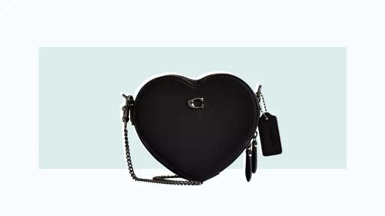 A black leather crossbody bag in the shape of a heart.