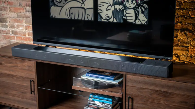The all black Sony HT-A7000 sits atop a dark wood console against a brick wall below a large flat screen TV as Shutter Island plays.