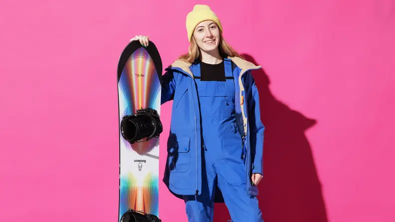 woman holding snowboard in front of pink background