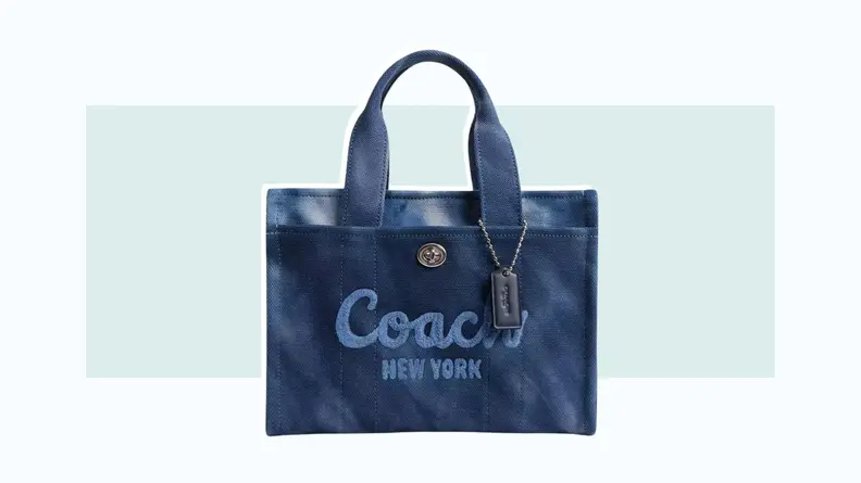 A canvas tote bag in blue tie-dye fabric, with the Coach logo across the front.
