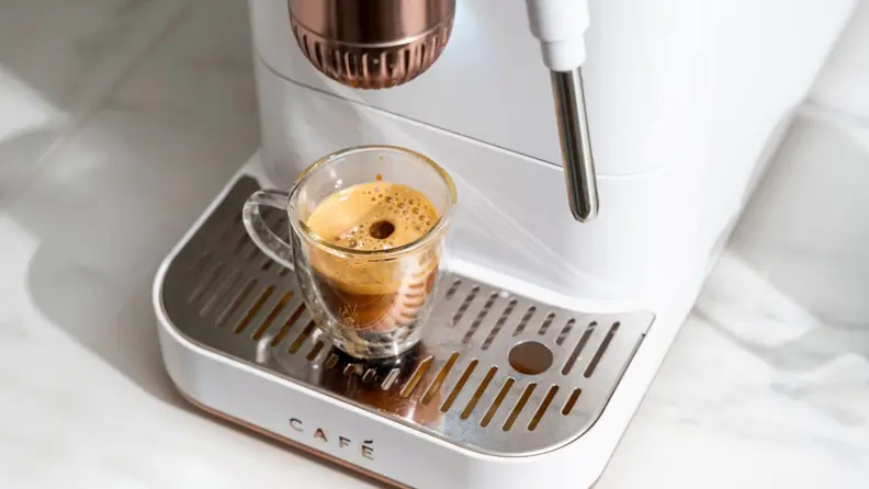 Close-up of Affetto machine pouring crema-topped espresso into a glass shot mug with a drop on top.