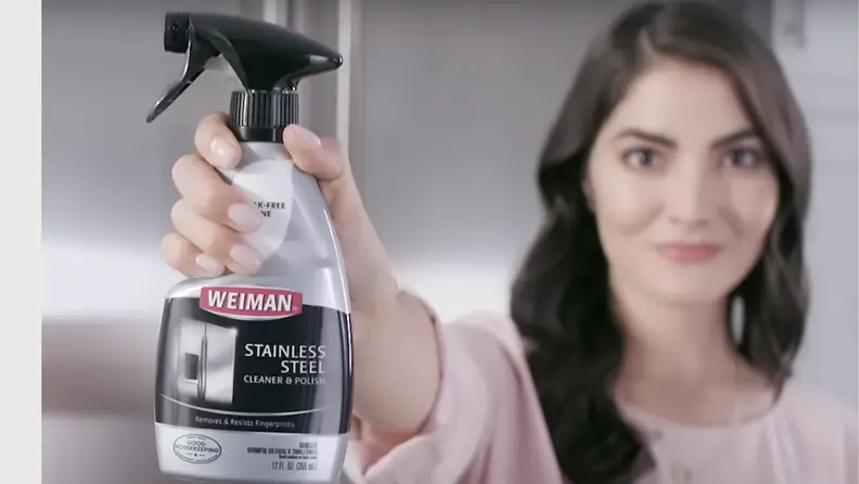 Weiman stainless steel cleaner spray focused on the image with a lady, blurred in the background, holding the cleaner
