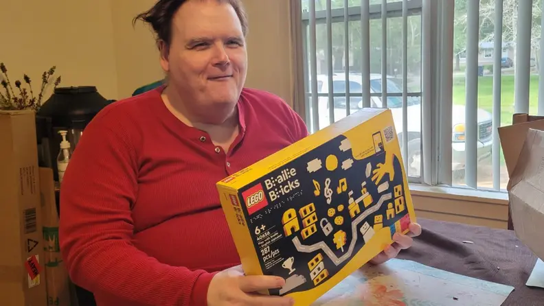A man holding the Lego Braille Bricks packaging box.