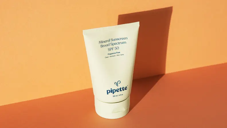 A light green tube of sunscreen stands on an orange backdrop.