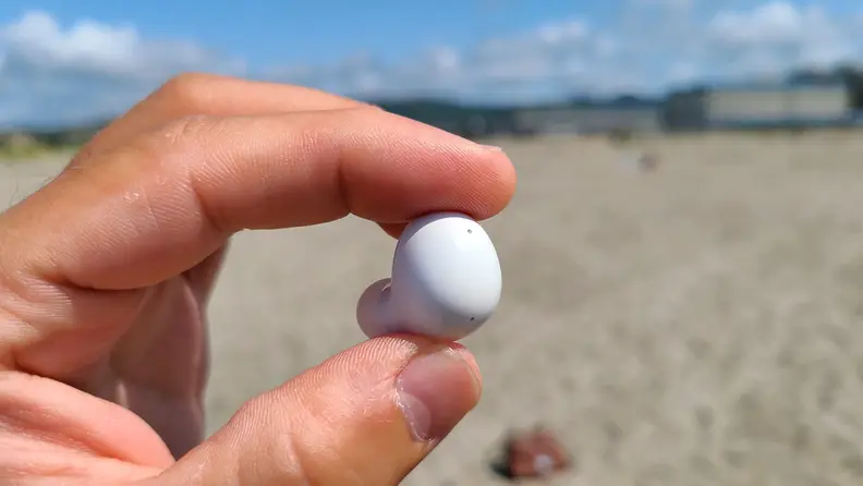 Samsung Galaxy Buds 2 is shown against a sunny beach.