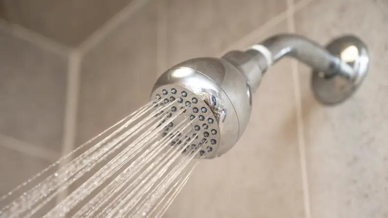The Wassa High Pressure shower head spraying water in a shower with beige tile.