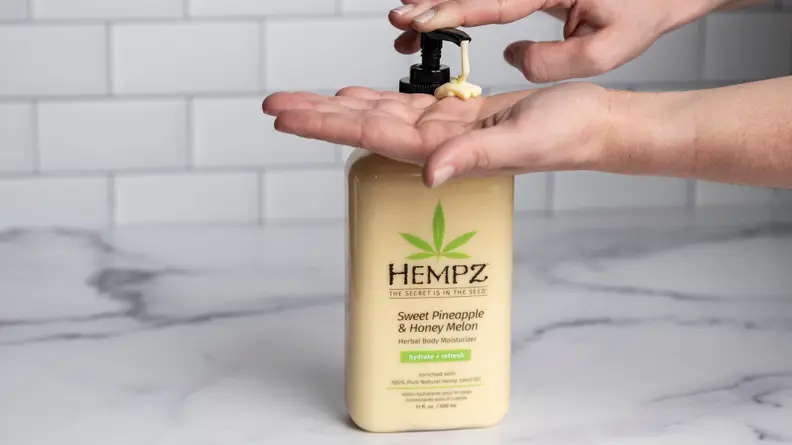 A person's hand pumping a yellow bottle of body lotion.