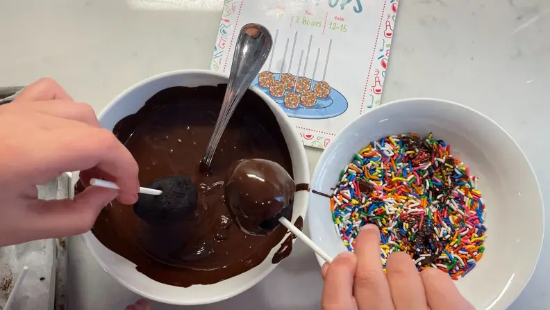 A child dips a cap pop in melted chocolate.