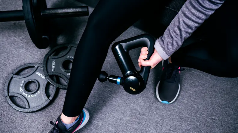 A Theragun Elite is used to massage a calf leg, and could be one of the best birthday gifts for Aries season.