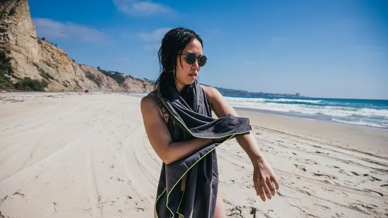 A woman dries off her arm with a grey beach towel.