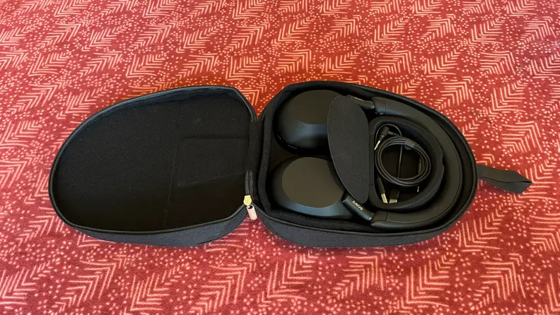 The black Sony WH-1000XM5 sit on a red table with an open case