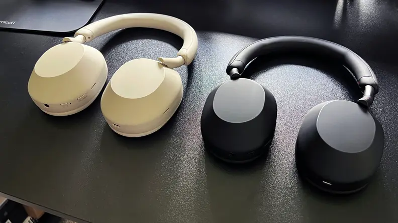 Sony WH-1000XM5 white and black models sit on a black desktop