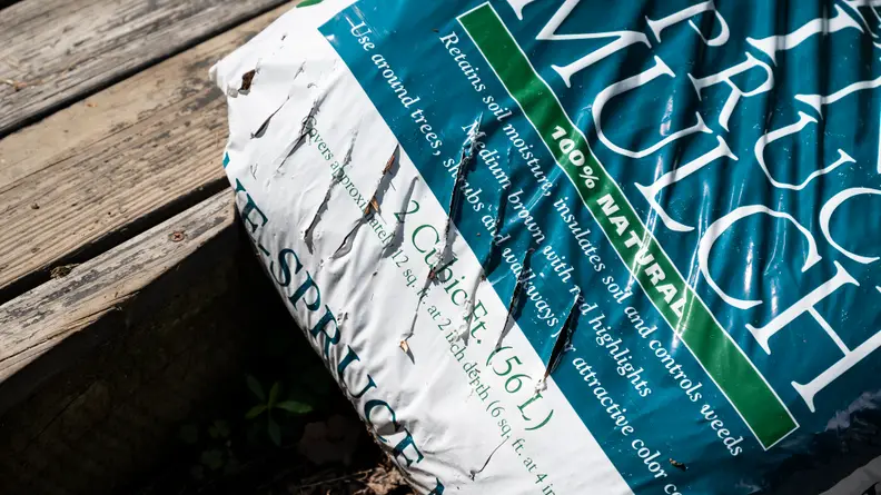 A mulch bag lies across a porch. It has slashes cut along its side.
