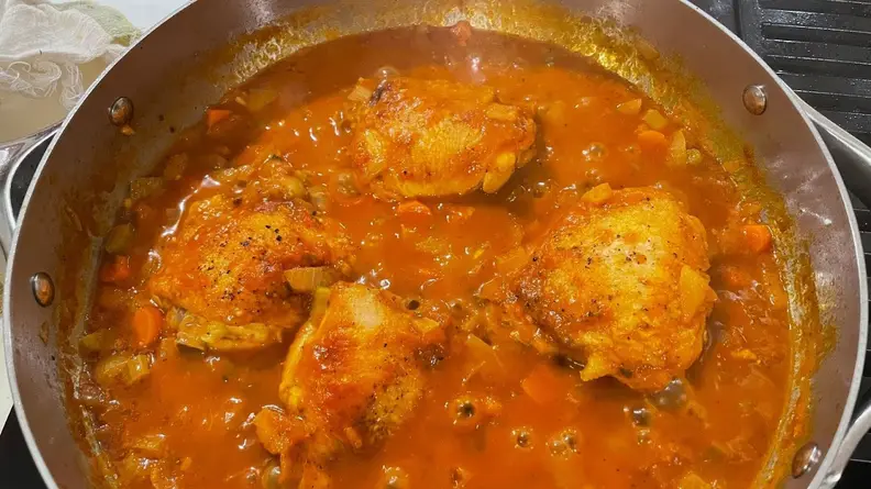 Chicken thighs cooking in orange sauce inside of stainless steel pan.