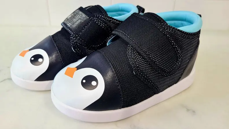 A top-side view of penguin-design Ikiki shoes on a marble floor