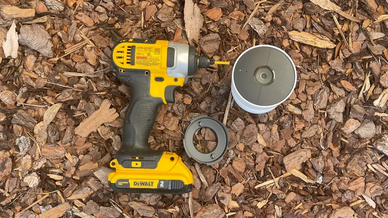 A drill, mounting base with screws, and the new Nest Cam sit on a pile of mulch.
