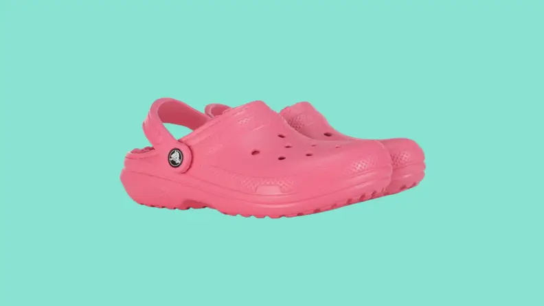 Side view of a pair of pink fuzz-lined Crocs on a dark teal background.