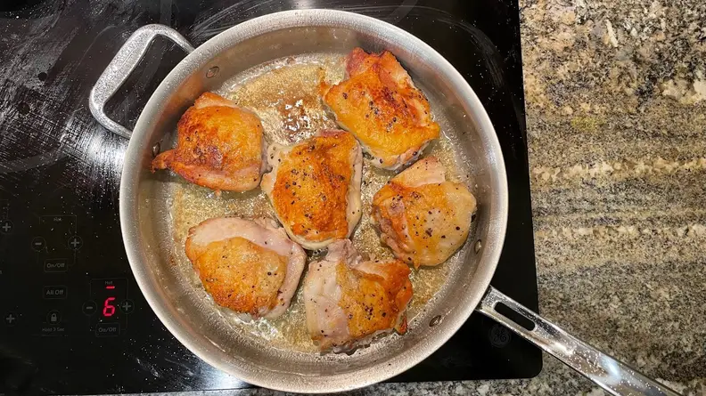 Chicken thighs searing in an All Clad stainless steel pan