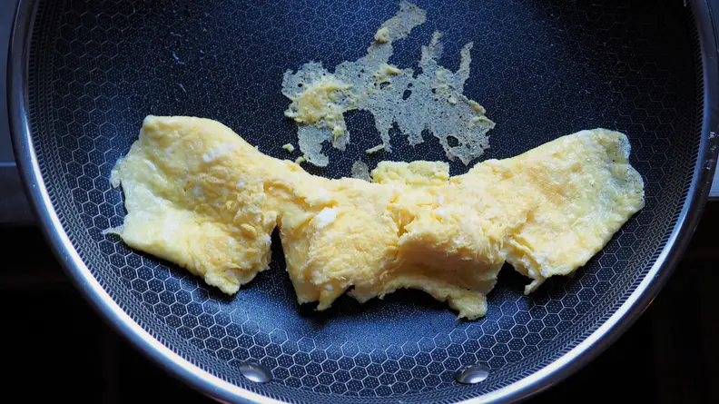 A French omelet slides down a pan, leaving bits behind to evaluate the pan's nonstick properties.