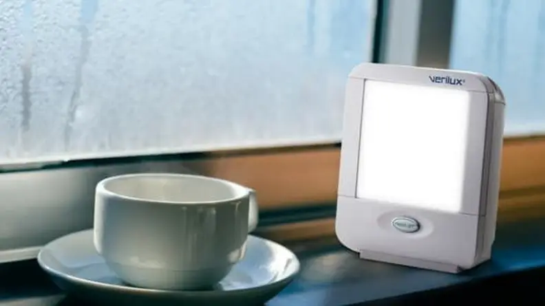 The Verilux Portable Light Therapy Lamp on a windowsill, next to a teacup.