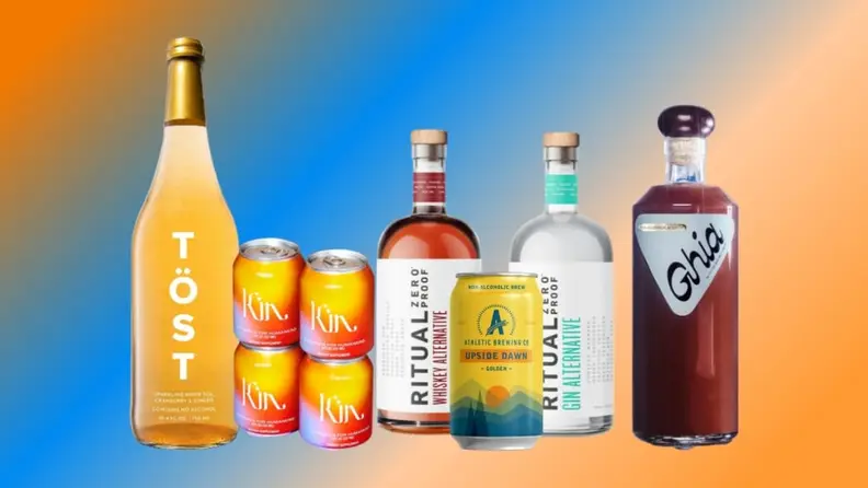 Bottles of several brands of zero-proof cocktail, wine, and liqueur lined up on a colorful, blurry background.