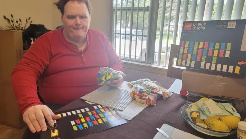 A man opening the Lego Braille Bricks packaging.
