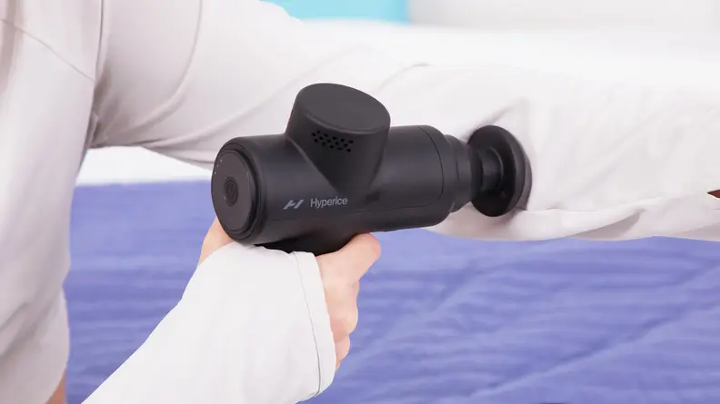A woman taking the Hyperice Hypervolt 2 Go on her arm.